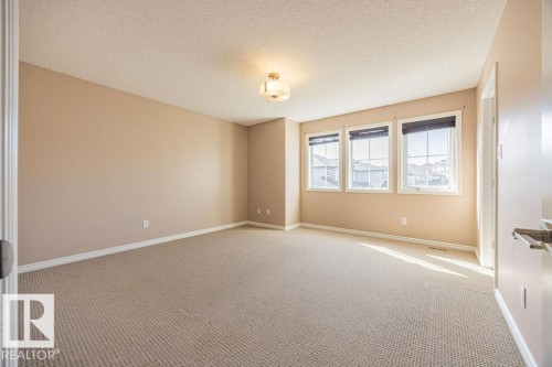 Spacious room featuring neutral wall paint, light-toned textured carpeting, three transom windows with blinds, a white trim package, and an overhead flush-mount light fixture - 14 9350 211 Street, Edmonton, AB - Indoor Photo Showing Other Room