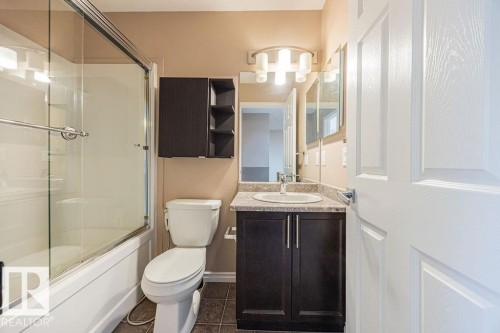 Bathroom featuring a shower-tub combination with glass enclosure, dark wood-finish vanity with countertop sink, wall-mounted mirrored medicine cabinet, and tiled flooring - 14 9350 211 Street, Edmonton, AB - Indoor Photo Showing Bathroom