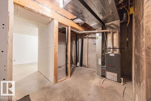 Unfinished basement space featuring a visible furnace unit, concrete flooring, exposed ceiling joists, and framed doorways - 14 9350 211 Street, Edmonton, AB - Indoor Photo Showing Basement