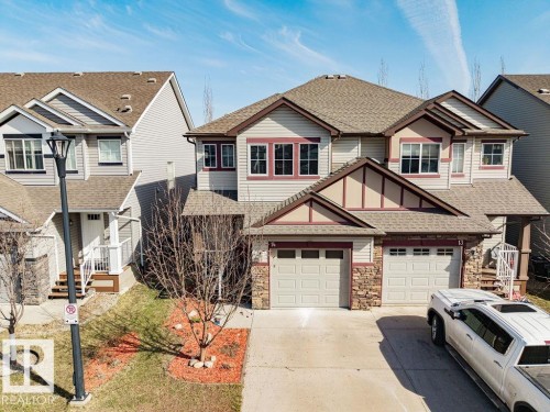 Two-story residence featuring light-colored siding, a stone facade accent, and a dual garage with carriage-style doors - 14 9350 211 Street, Edmonton, AB - Outdoor