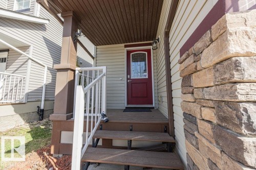 Welcoming front entrance featuring a red paneled door with decorative glass, stone veneer accent, wood-finish porch steps, white railing, and a covered entryway with a soffit ceiling - 14 9350 211 Street, Edmonton, AB - Outdoor With Exterior