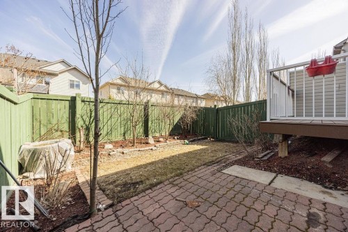 Enclosed backyard featuring a red paver patio, a raised wood deck with white railings, and green privacy fencing - 14 9350 211 Street, Edmonton, AB - Outdoor