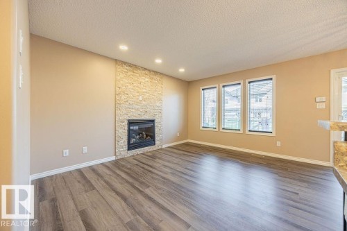 Contemporary living area featuring a stacked stone fireplace with a black insert - 14 9350 211 Street, Edmonton, AB - Indoor Photo Showing Living Room With Fireplace