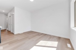 Spacious room featuring light wood-finish flooring, crisp white walls, and a large window - 