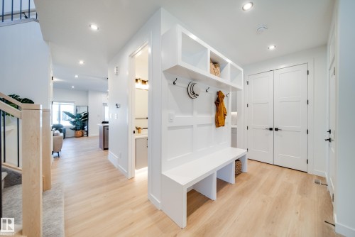 Entryway featuring a built-in bench with integrated shelving and wall hooks, light wood-finish flooring, recessed lighting, and white paneled doors with matte black hardware - 16 Blackbird Bend, Fort Saskatchewan, AB - Indoor Photo Showing Other Room