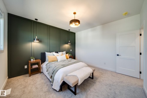 Bedroom featuring a dark green accent wall with vertical paneling, contemporary pendant lighting, and a modern ceiling fixture - 16 Blackbird Bend, Fort Saskatchewan, AB - Indoor Photo Showing Bedroom