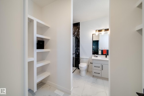 Bathroom featuring marble-look flooring, a white vanity with a rectangular sink, a black-framed mirror, and a black-tiled shower with a clear glass enclosure - 16 Blackbird Bend, Fort Saskatchewan, AB - Indoor