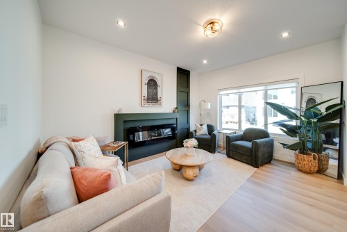 Spacious living area featuring light wood-finish flooring, recessed lighting, a modern built-in fireplace with a dark green surround, and a large window providing natural illumination - 16 Blackbird Bend, Fort Saskatchewan, AB - Indoor Photo Showing Living Room With Fireplace