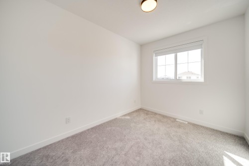 Bright interior space featuring a double-paned window, neutral carpet flooring, white walls, white trim, and an overhead flush-mount light fixture - 16 Blackbird Bend, Fort Saskatchewan, AB - Indoor Photo Showing Other Room