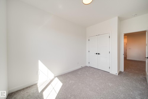 Carpeted room featuring a double-door closet with black hardware, white baseboards, and a flush-mount ceiling light fixture - 16 Blackbird Bend, Fort Saskatchewan, AB - Indoor Photo Showing Other Room