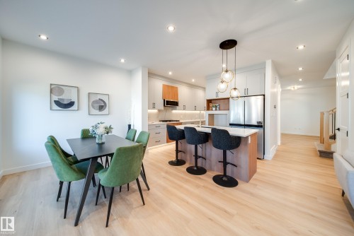 Open-concept kitchen featuring light wood-finish flooring, white cabinetry, a built-in stainless steel refrigerator, and a kitchen island with a waterfall countertop - 16 Blackbird Bend, Fort Saskatchewan, AB - Indoor