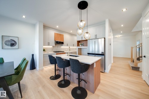 Open-concept kitchen featuring light wood-finish flooring, a central island with a light-toned countertop, and stainless steel appliances - 16 Blackbird Bend, Fort Saskatchewan, AB - Indoor