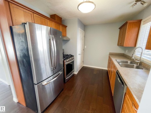 Kitchen featuring wood-finish flooring, stainless steel appliances, wood cabinetry, a double basin sink, and a countertop - 5806 118 Avenue Nw, Edmonton, AB - Indoor Photo Showing Kitchen With Double Sink