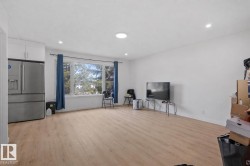 Spacious room featuring light wood-finish flooring, recessed lighting, and a large window with blue drapes - 