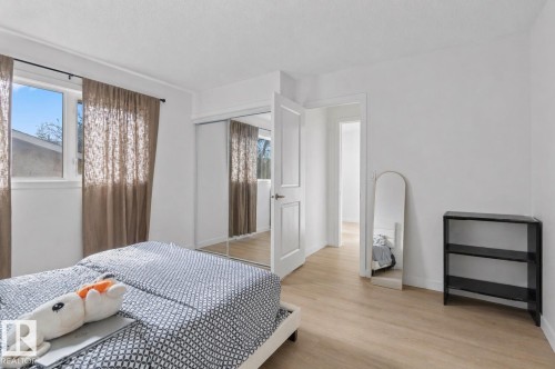 Bedroom featuring wood-finish flooring, a double window, and a sliding mirrored closet door - 1566 Lakewood Road Nw, Edmonton, AB - Indoor Photo Showing Bedroom