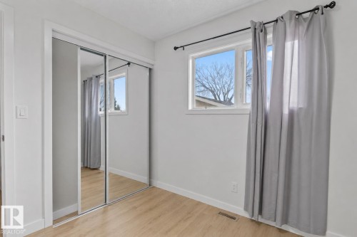 Mirrored sliding closet doors with white trim, wood-finish flooring, and a window with white casing - 1566 Lakewood Road Nw, Edmonton, AB - Indoor Photo Showing Other Room