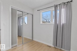 Mirrored sliding closet doors with white trim, wood-finish flooring, and a window with white casing - 