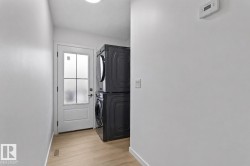 Dedicated laundry area featuring stacked appliances, wood-finish flooring, a white paneled door with frosted glass, and a flush-mount ceiling light - 