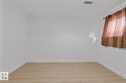 Spacious room featuring light wood-finish flooring, white walls, and a window with brown sheer drapes - 