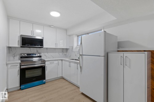Contemporary kitchen featuring white cabinetry, light countertops, and a white backsplash - 1566 Lakewood Road Nw, Edmonton, AB - Indoor Photo Showing Kitchen
