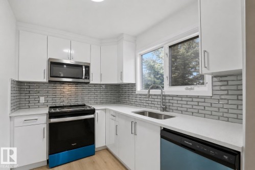 Modern kitchen featuring white cabinetry, light-toned countertops, a full subway tile backsplash, stainless steel appliances, and a window above the sink - 1566 Lakewood Road Nw, Edmonton, AB - Indoor Photo Showing Kitchen With Upgraded Kitchen