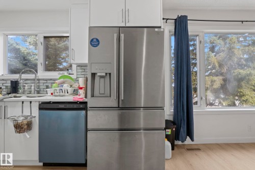 Stainless steel French-door refrigerator, white upper and lower cabinetry, light-toned wood-finish flooring, and a tile backsplash - 1566 Lakewood Road Nw, Edmonton, AB - Indoor Photo Showing Kitchen