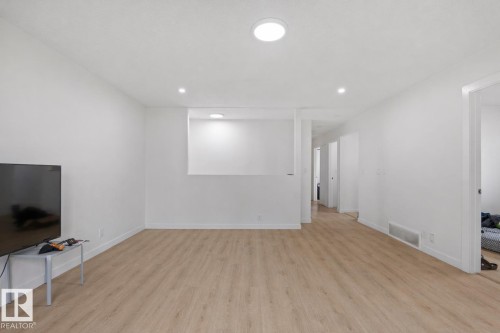 Spacious interior featuring light wood-finish flooring, recessed lighting, white baseboards, and a built-in wall niche with accent lighting - 1566 Lakewood Road Nw, Edmonton, AB - Indoor Photo Showing Other Room