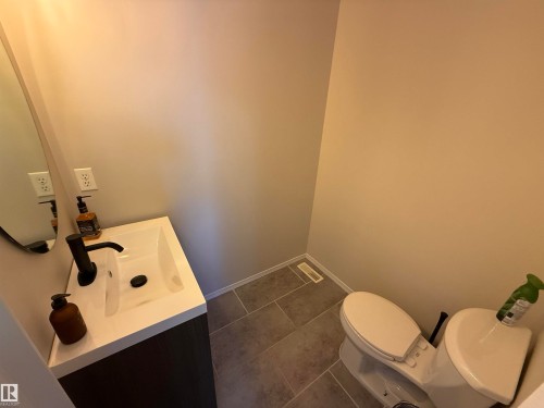 Powder room featuring a dark wood-finish vanity with an integrated white sink, matte black faucet, and a wall-mounted oval mirror - 97 2021 Grantham Crest, Edmonton, AB - Indoor Photo Showing Bathroom