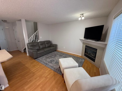 Living area featuring wood-finish flooring, a corner fireplace with tile surround and mantel, and a window with blinds - 97 2021 Grantham Crest, Edmonton, AB - Indoor Photo Showing Living Room With Fireplace