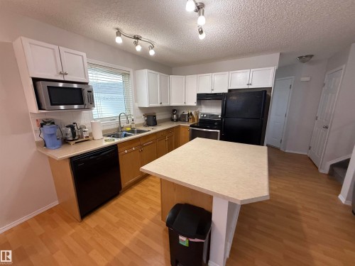 Kitchen featuring a peninsula with countertop seating, wood-finish flooring, white upper cabinetry, and a stainless steel over-the-range microwave - 97 2021 Grantham Crest, Edmonton, AB - Indoor Photo Showing Kitchen With Double Sink