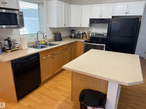 Kitchen featuring wood-finish flooring, two-tone cabinetry, a stainless steel microwave, black dishwasher, and a freestanding island with countertop - 97 2021 Grantham Crest, Edmonton, AB - Indoor Photo Showing Kitchen With Double Sink