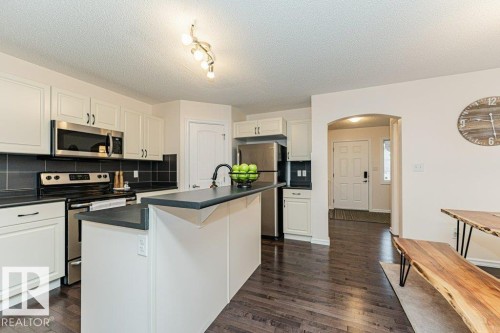 The property features a bright kitchen with white cabinetry, stainless steel appliances, and dark countertops, complemented by dark wood flooring - 2828 21 Avenue, Edmonton, AB - Indoor Photo Showing Kitchen With Stainless Steel Kitchen