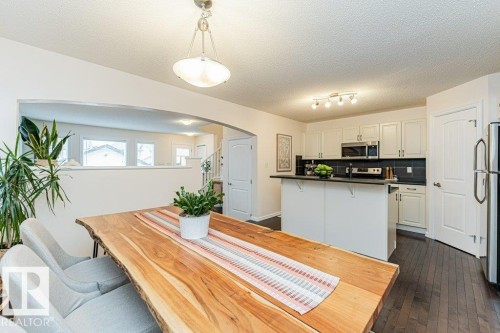 The dining area features a large light wood table, with a view of the kitchen which includes white cabinetry, dark countertops, and stainless steel appliances - 2828 21 Avenue, Edmonton, AB - Indoor