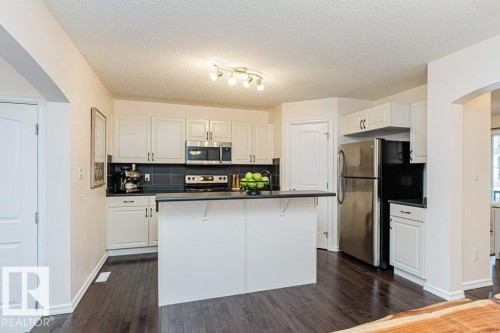Kitchen featuring white cabinetry, dark countertops, dark backsplash, stainless steel appliances, and dark hardwood flooring - 2828 21 Avenue, Edmonton, AB - Indoor Photo Showing Kitchen