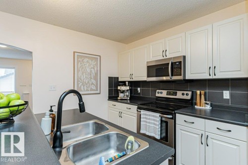 The kitchen features a double basin stainless steel sink, a black faucet, white cabinetry with black handles, and a stainless steel oven and microwave - 2828 21 Avenue, Edmonton, AB - Indoor Photo Showing Kitchen With Double Sink