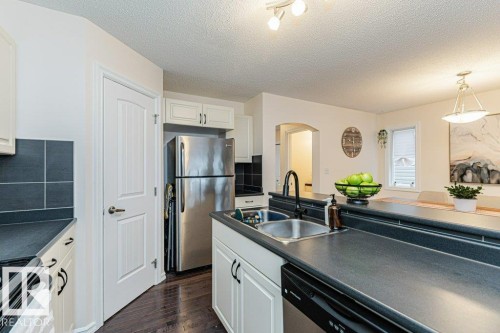 The kitchen features white cabinetry, dark countertops, a double basin stainless steel sink, a stainless steel refrigerator, and dark wood flooring - 2828 21 Avenue, Edmonton, AB - Indoor Photo Showing Kitchen With Double Sink
