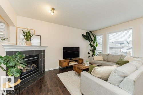 Living area featuring dark hardwood floors, a fireplace with dark tile surround, and windows with blinds - 2828 21 Avenue, Edmonton, AB - Indoor Photo Showing Living Room With Fireplace