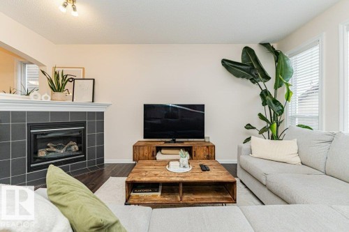 Bright living area featuring dark wood flooring, a fireplace with dark grey tile surround, and large windows with blinds - 2828 21 Avenue, Edmonton, AB - Indoor Photo Showing Living Room With Fireplace