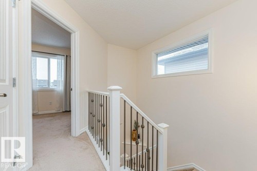A bright hallway featuring neutral carpeting, a white staircase with decorative metal spindles, and a rectangular window providing natural illumination - 2828 21 Avenue, Edmonton, AB - Indoor Photo Showing Other Room