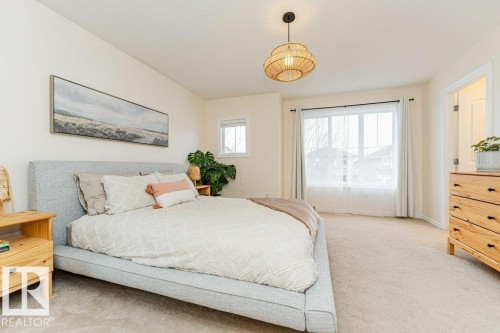 This bedroom features carpeted flooring, a large window with sheers, and a contemporary ceiling fixture - 2828 21 Avenue, Edmonton, AB - Indoor Photo Showing Bedroom