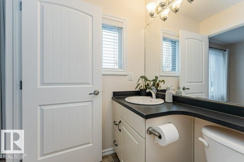 Bathroom featuring a light beige vanity with a black countertop and an integrated sink, a large mirror, and a window with blinds - 2828 21 Avenue, Edmonton, AB - Indoor Photo Showing Bathroom