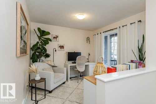 This versatile space features a large window with white curtains, a neutral wall color, and a textured area rug - 2828 21 Avenue, Edmonton, AB - Indoor