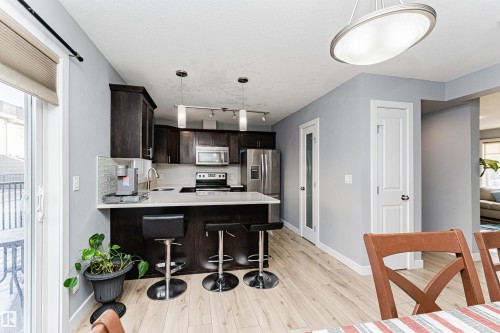 Kitchen featuring dark wood cabinetry, stainless steel appliances, a white subway tile backsplash, and light wood flooring - 35 675 Albany Way Nw, Edmonton, AB - Indoor