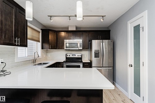 The kitchen features dark wood cabinetry, white countertops, stainless steel appliances, and a tiled backsplash - 35 675 Albany Way Nw, Edmonton, AB - Indoor Photo Showing Kitchen With Double Sink With Upgraded Kitchen