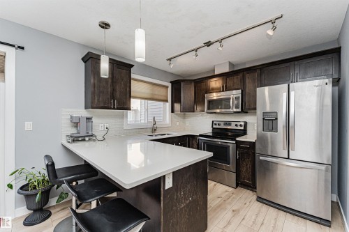 The kitchen features dark wood cabinetry, stainless steel appliances, and light-colored countertops - 35 675 Albany Way Nw, Edmonton, AB - Indoor Photo Showing Kitchen With Upgraded Kitchen