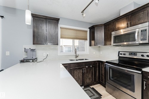 The kitchen features dark wood cabinetry, stainless steel appliances, and light-colored countertops - 35 675 Albany Way Nw, Edmonton, AB - Indoor Photo Showing Kitchen With Double Sink With Upgraded Kitchen
