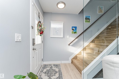 Entryway featuring light hardwood flooring, a white paneled door with glass inserts, and a staircase with carpeted treads and a glass railing - 35 675 Albany Way Nw, Edmonton, AB - Indoor Photo Showing Other Room