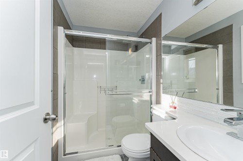 This bathroom features a contemporary shower enclosure with glass doors, a white vanity with an integrated sink, and a large mirror - 35 675 Albany Way Nw, Edmonton, AB - Indoor Photo Showing Bathroom