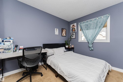 This room features a window providing natural light, a bed with a dark headboard, and a desk area - 35 675 Albany Way Nw, Edmonton, AB - Indoor Photo Showing Bedroom