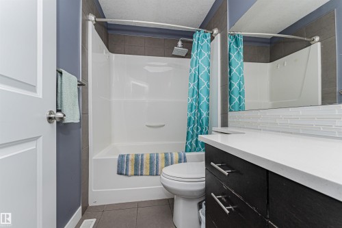 Bathroom featuring a white bathtub and shower combination with dark gray tiled walls and a rain shower head - 35 675 Albany Way Nw, Edmonton, AB - Indoor Photo Showing Bathroom